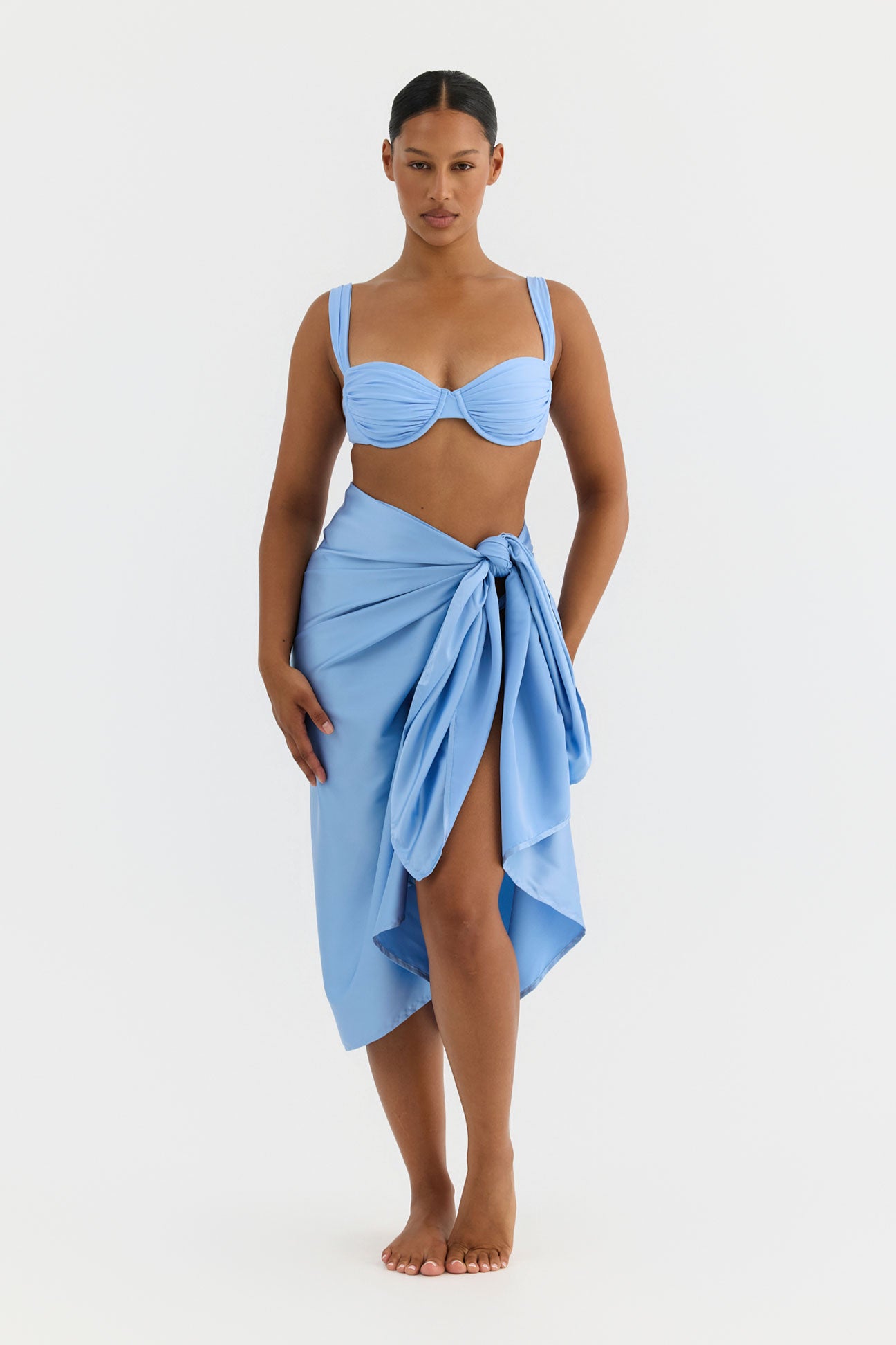 Woman wearing a light blue bikini with a matching sarong on a white background
