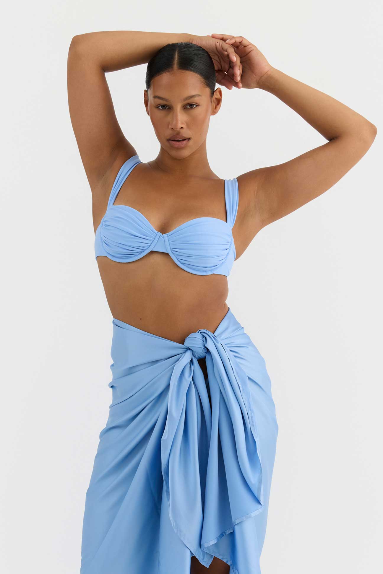 Woman wearing a light blue bikini with a matching sarong on a white background
