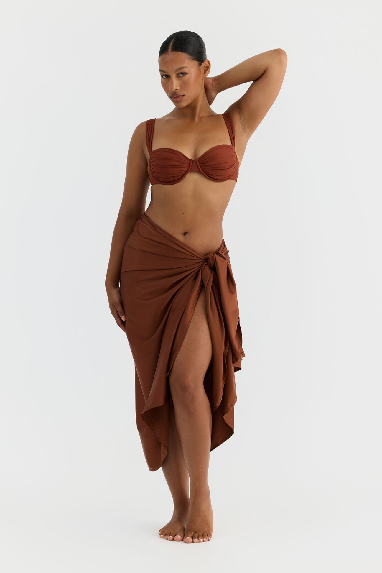 Woman wearing a terracotta bikini with a matching wrap skirt on a white background