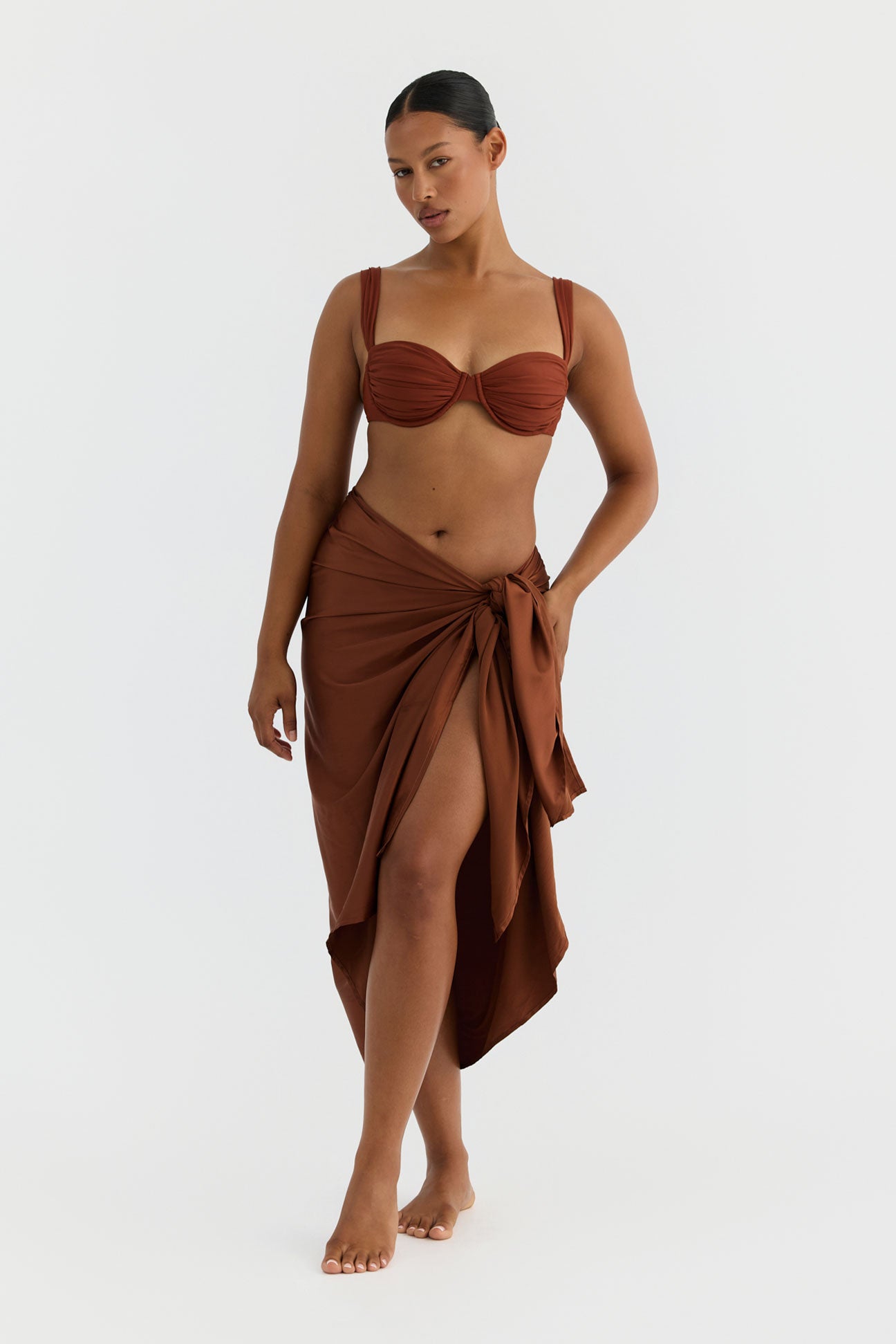 Woman wearing a terracotta bikini with a matching wrap skirt on a white background