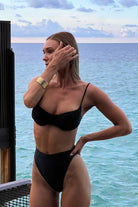 Woman in a black bikini standing by the ocean with a scenic view.