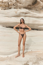 Woman in a black bikini standing against a textured rock wall.