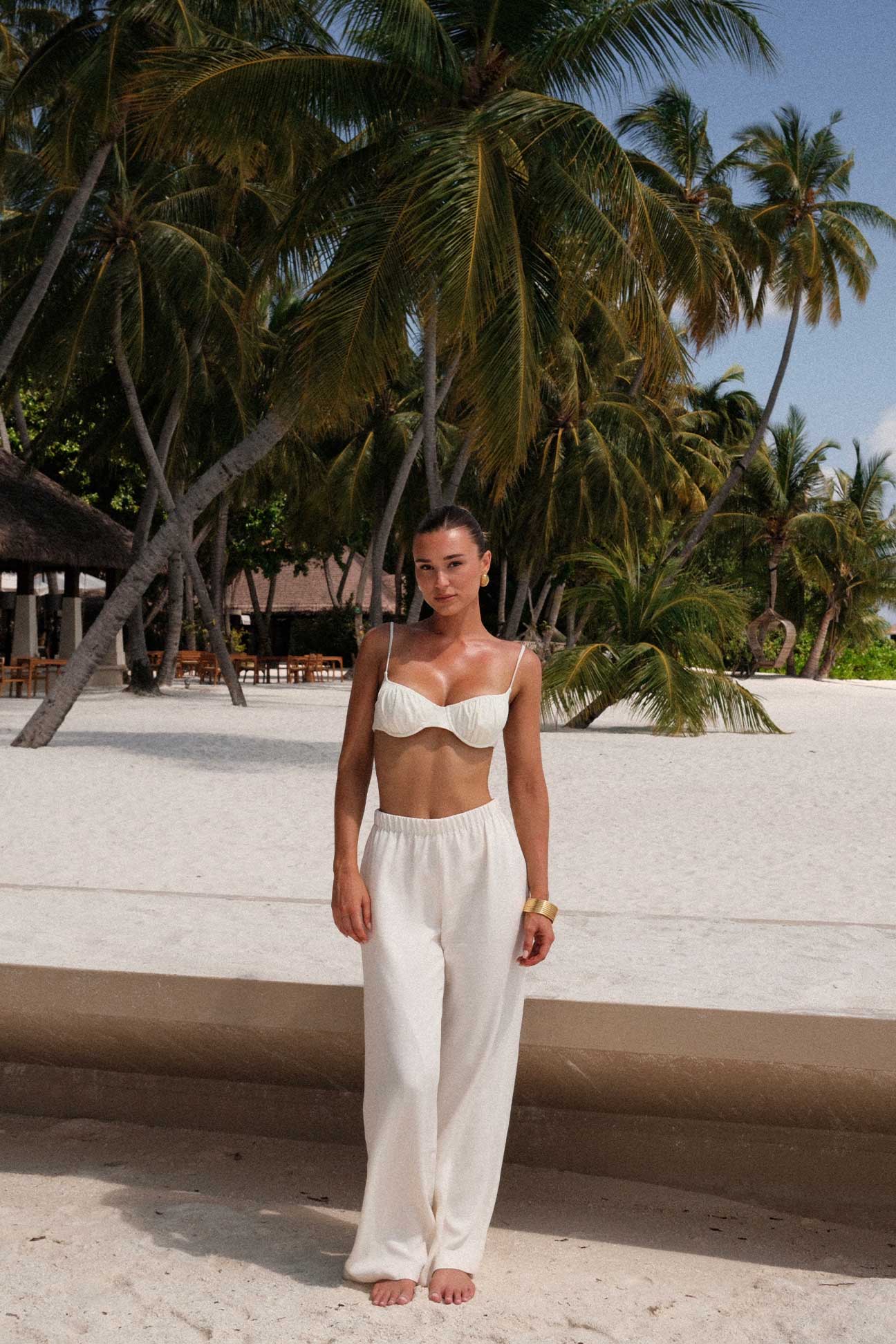 Woman in a white bikini top and pants standing in front of palm trees