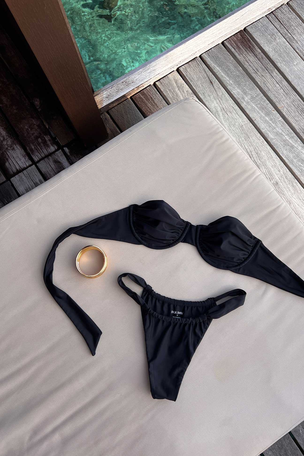Black bikini set on a white surface with a blurred pool background