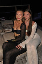 Two women sitting on a couch in matching bikini and dress sets.
