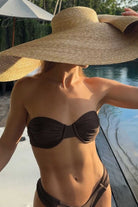 Person wearing a black bikini and large straw hat by a poolside.