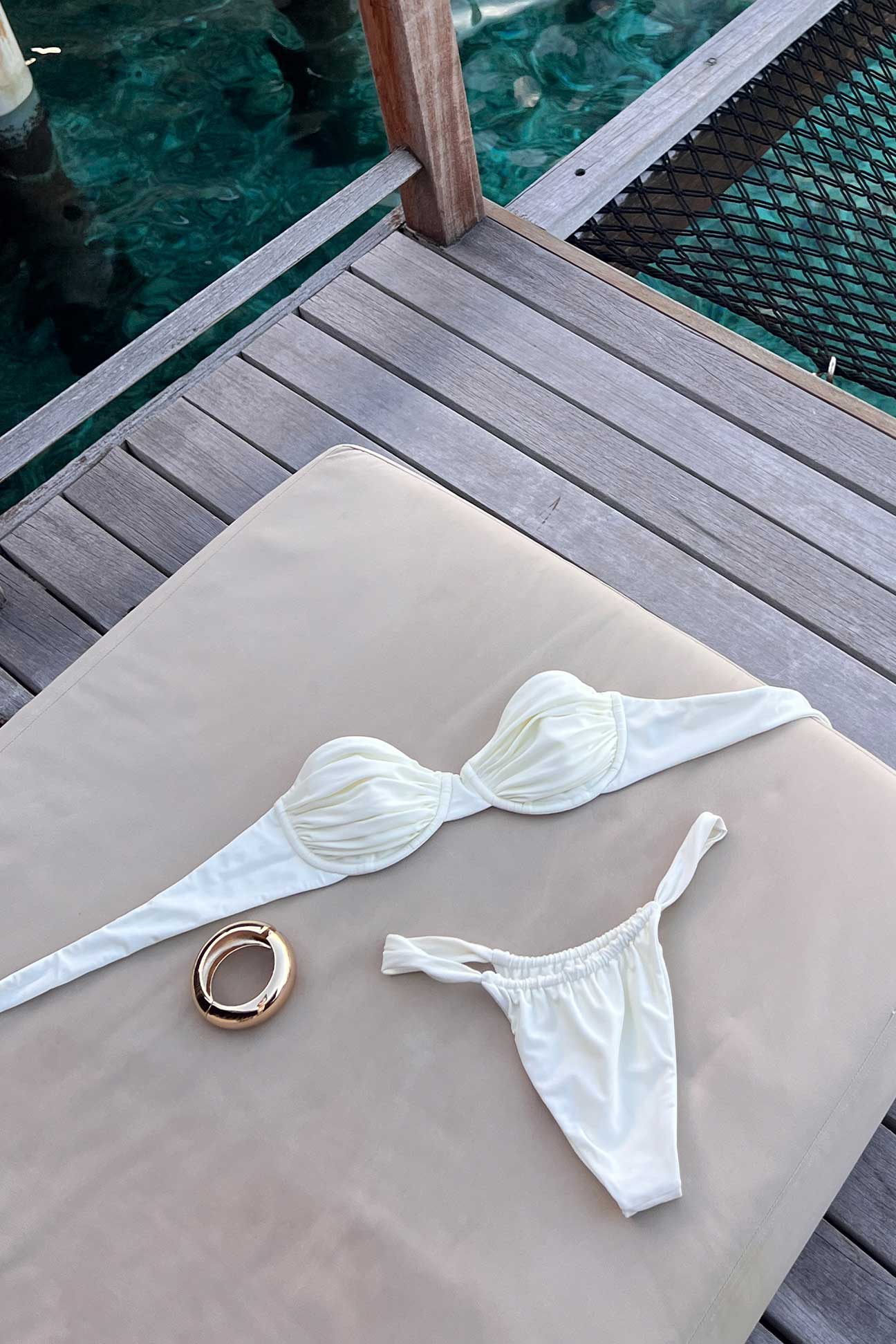 White bikini set on a wooden deck with a ring nearby