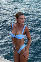 Woman in a blue bikini standing by the ocean