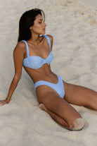 Woman in a light blue bikini sitting on a sandy beach