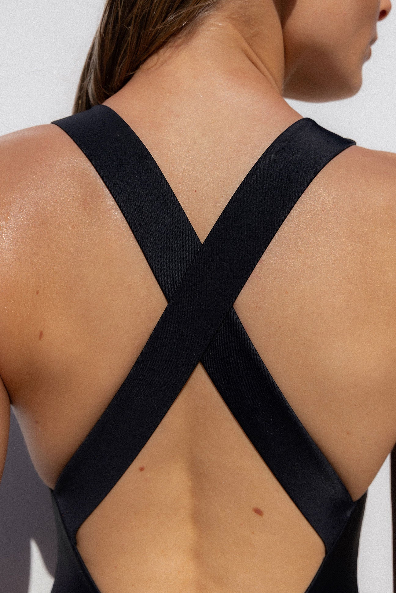 Close-up back view of a woman wearing a black strappy top with wide crisscross shoulder straps and an open back cutout.