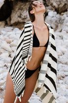 Woman in black bikini with a striped cover-up on a rocky beach
